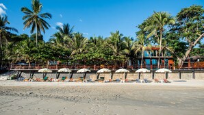 Une plage bordée de palmiers, un bâtiment avec un toit bleu et des chaises de plage sous des parasols.