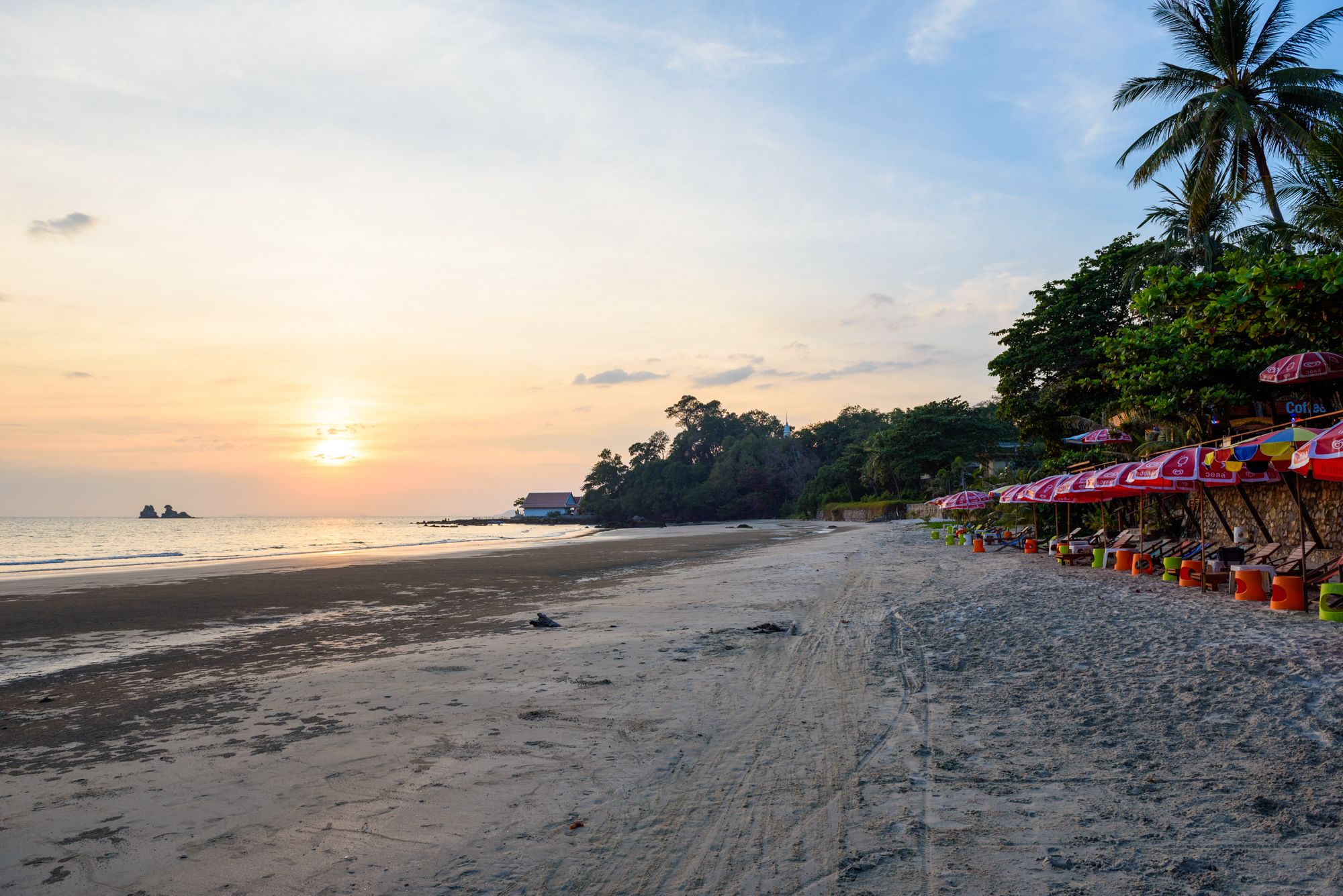 A beach with umbrellas and lounge chairs, a clear sky, and a sunset.