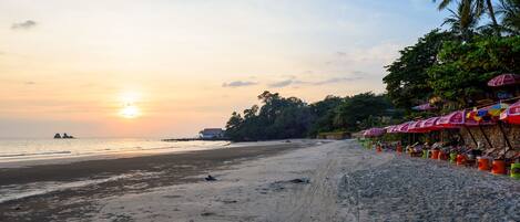 A beach with umbrellas and lounge chairs, a clear sky, and a sunset.
