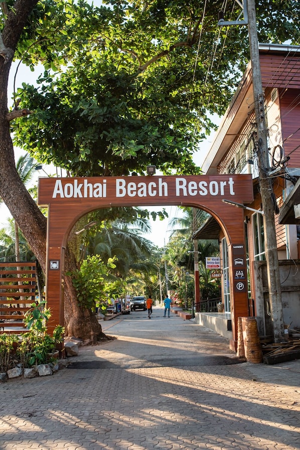 L’entrée du complexe hôtelier Aokhai Beach Resort se distingue par une arche en bois, un chemin pavé et la verdure environnante.