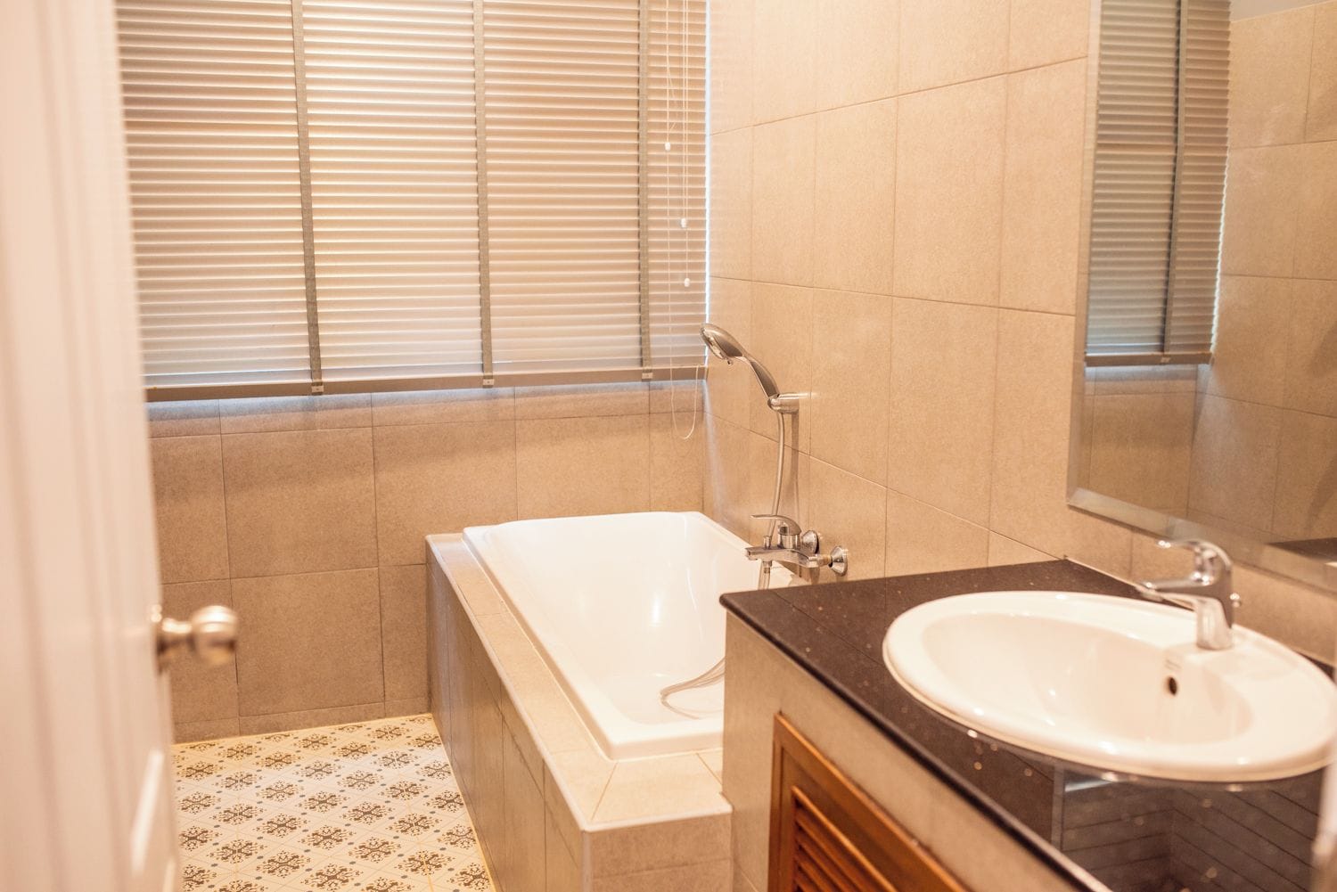 A bathroom with a bathtub, a sink, and a window with blinds.