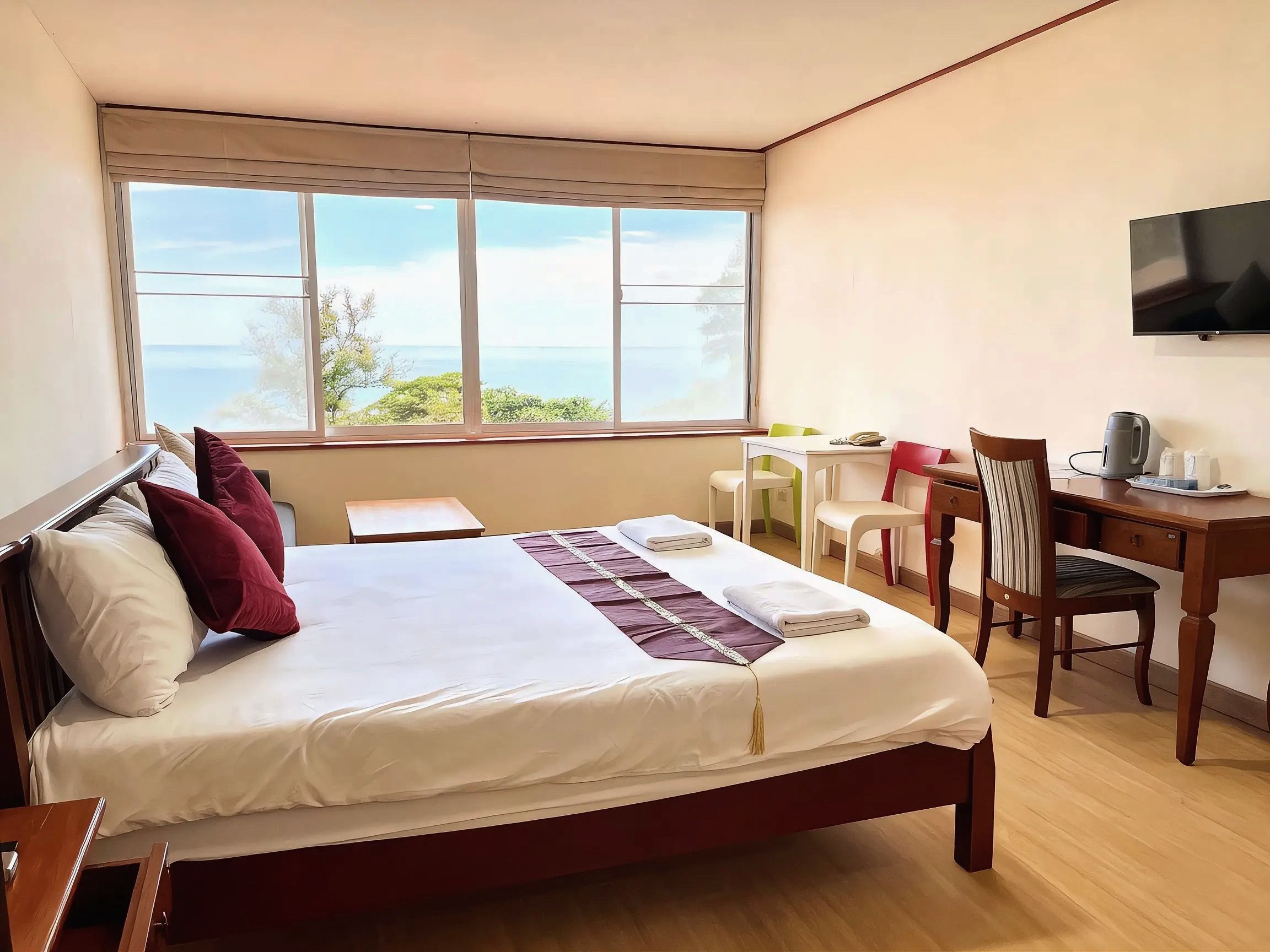 A hotel room with a bed, a desk, a chair, a television, and a window with a view of the sea.