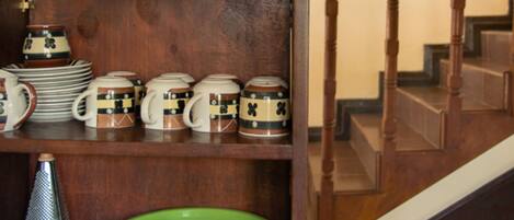 A wooden shelf with metal bowls, ceramic mugs, and a green bowl.