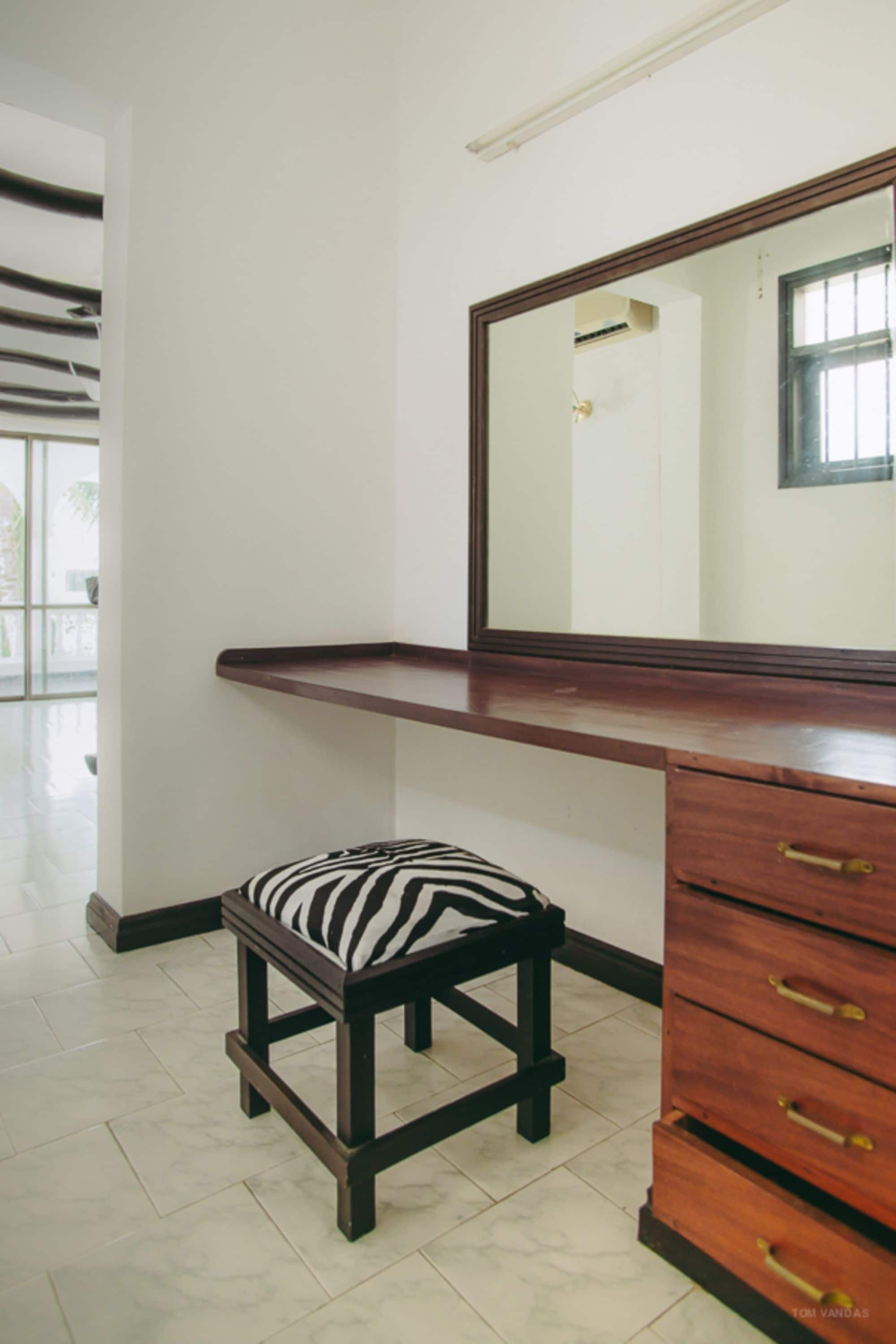 A room with a wooden vanity, a bench with a zebra pattern, and a large mirror.