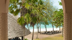 Een balkon met uitzicht op een strand, palmbomen en een hut met rieten dak.