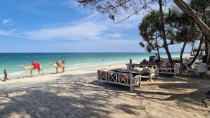 Een strand met kamelen, een houten terras en strandstoelen.