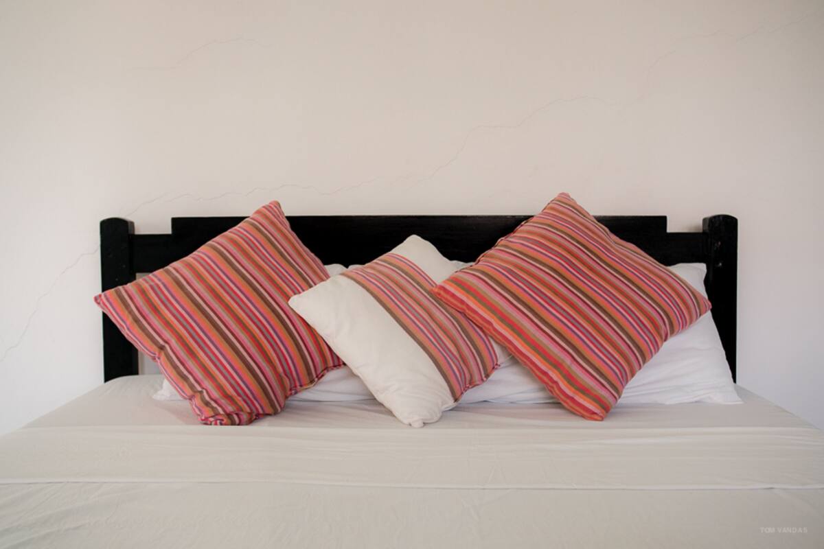 Una cama con cabecera negra, ropa de cama blanca y tres almohadas con estampados a rayas.