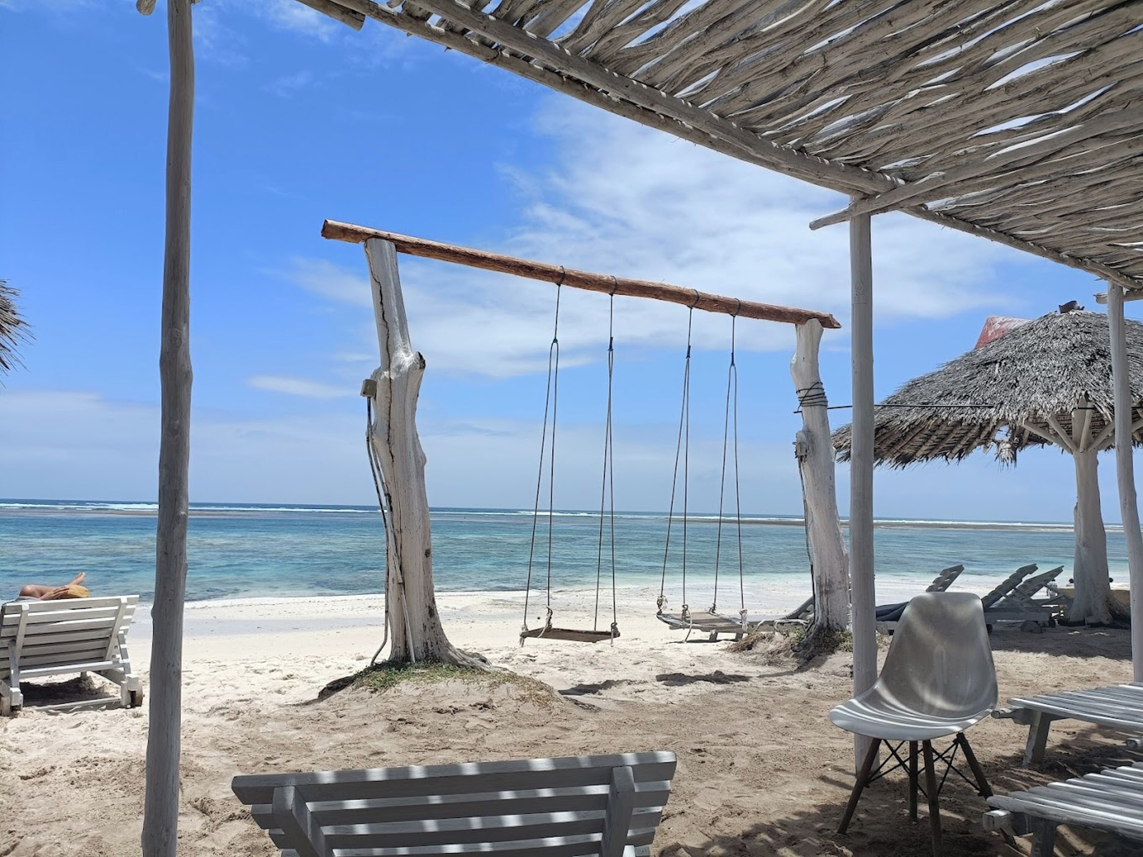 Ein Strand mit einer Holz-Schaukel, einer Bank und einem Gebäude mit einem Reetdach.