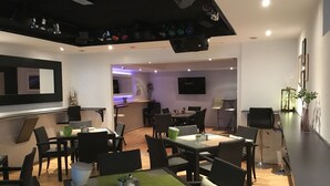 A modern dining area with multiple tables and chairs, a kitchen in the background, and a flat-screen TV mounted on the wall. - WohnRaum Hotel & Gästehaus (Gusterath)