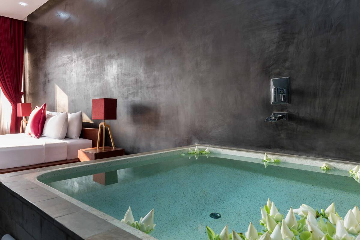 A modern spa area with a rectangular pool, a sofa with red cushions, and a wall-mounted control panel.