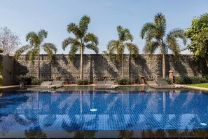 A swimming pool with tiled blue surface, surrounded by palm trees and stone walls. - Ung-D Hotel (Siem Reap)