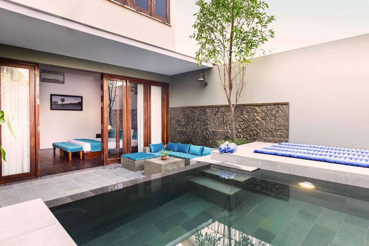 A modern outdoor pool area with a glass enclosure, blue cushioned seating, and a stone wall.