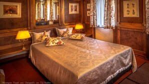 Una habitación de hotel con una cama grande, dos lámparas de noche, cortinas con motivos florales y obras de arte botánicas enmarcadas en las paredes.