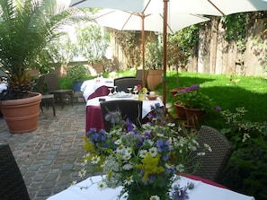 Patio esterno con tavolo apparecchiato per mangiare, circondato da piante in vaso e sedie.