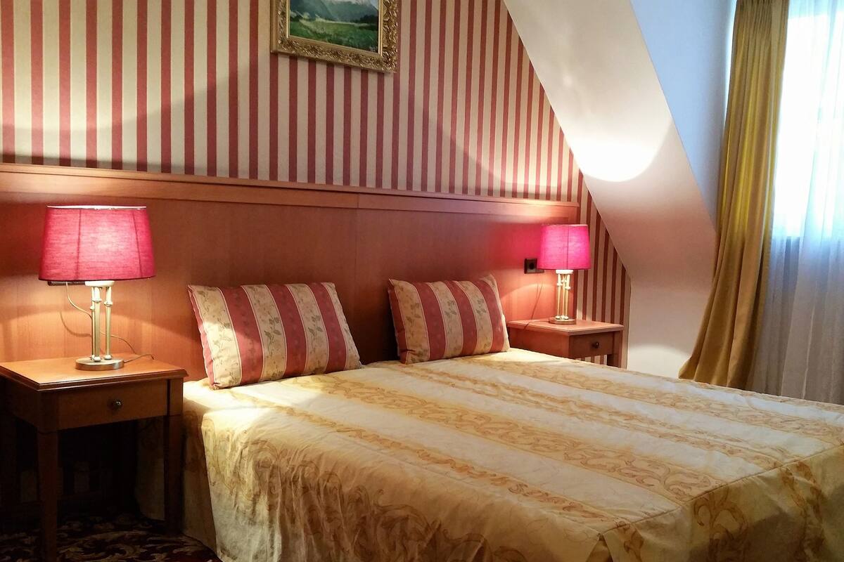 Ein Hotelzimmer mit einem Bett, zwei Nachttischen mit Lampen, einem Kopfteil und einem gerahmten Bild an der Wand.