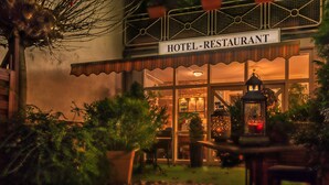 Restaurante de hotel con un letrero sobre la entrada, plantas en macetas y un farol.