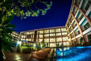 A multi-story hotel with a pool area, outdoor seating, and a well-lit facade. - Paragon Suites Resort (Pattaya)