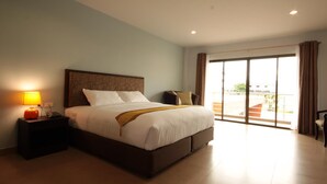 A hotel room with a bed, a nightstand with a lamp, a chair, and a view of the outside through a large window. - Paragon Suites Resort (Pattaya)