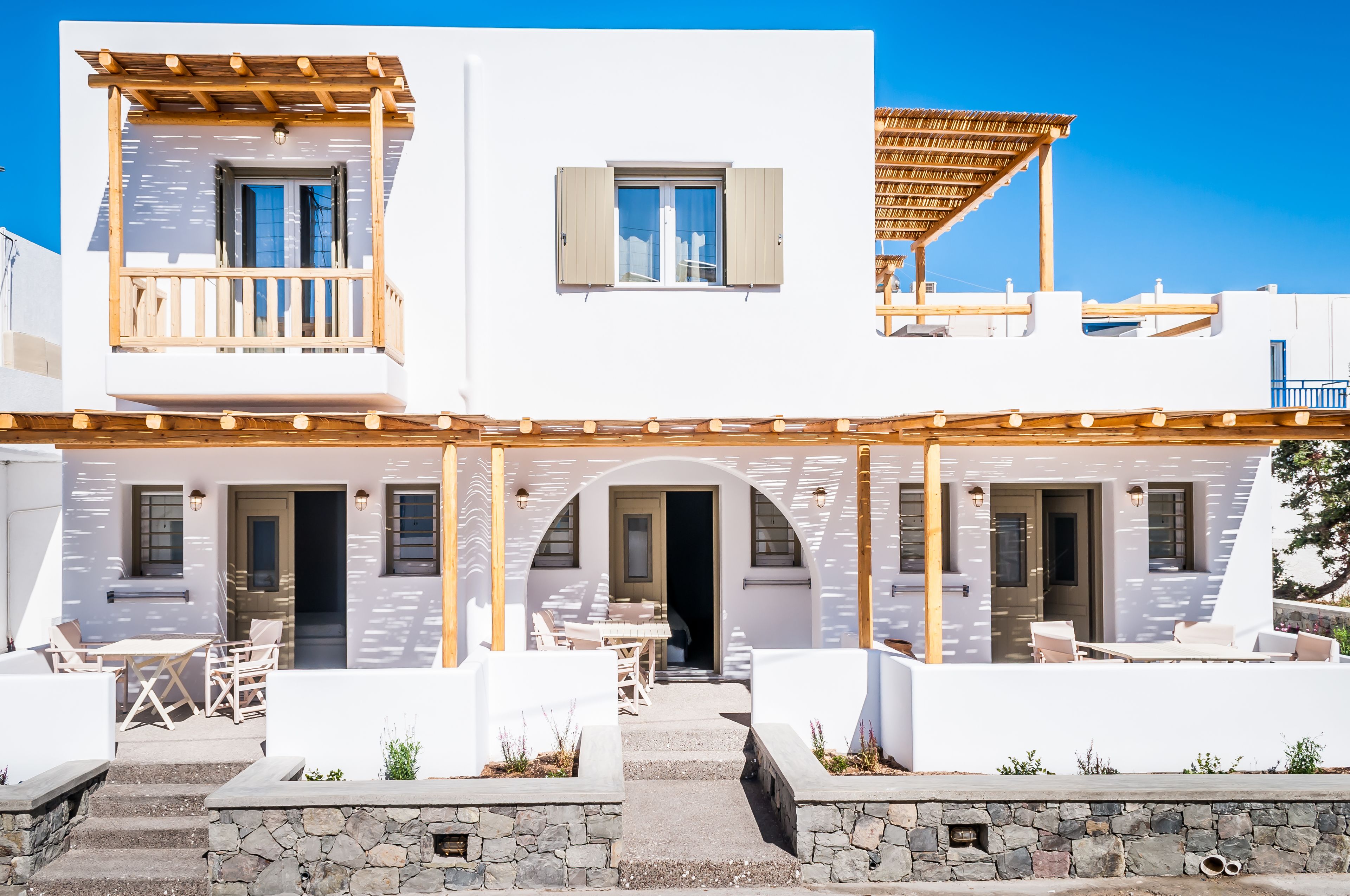 A two-story white building with a covered patio, stone steps, and outdoor seating.
