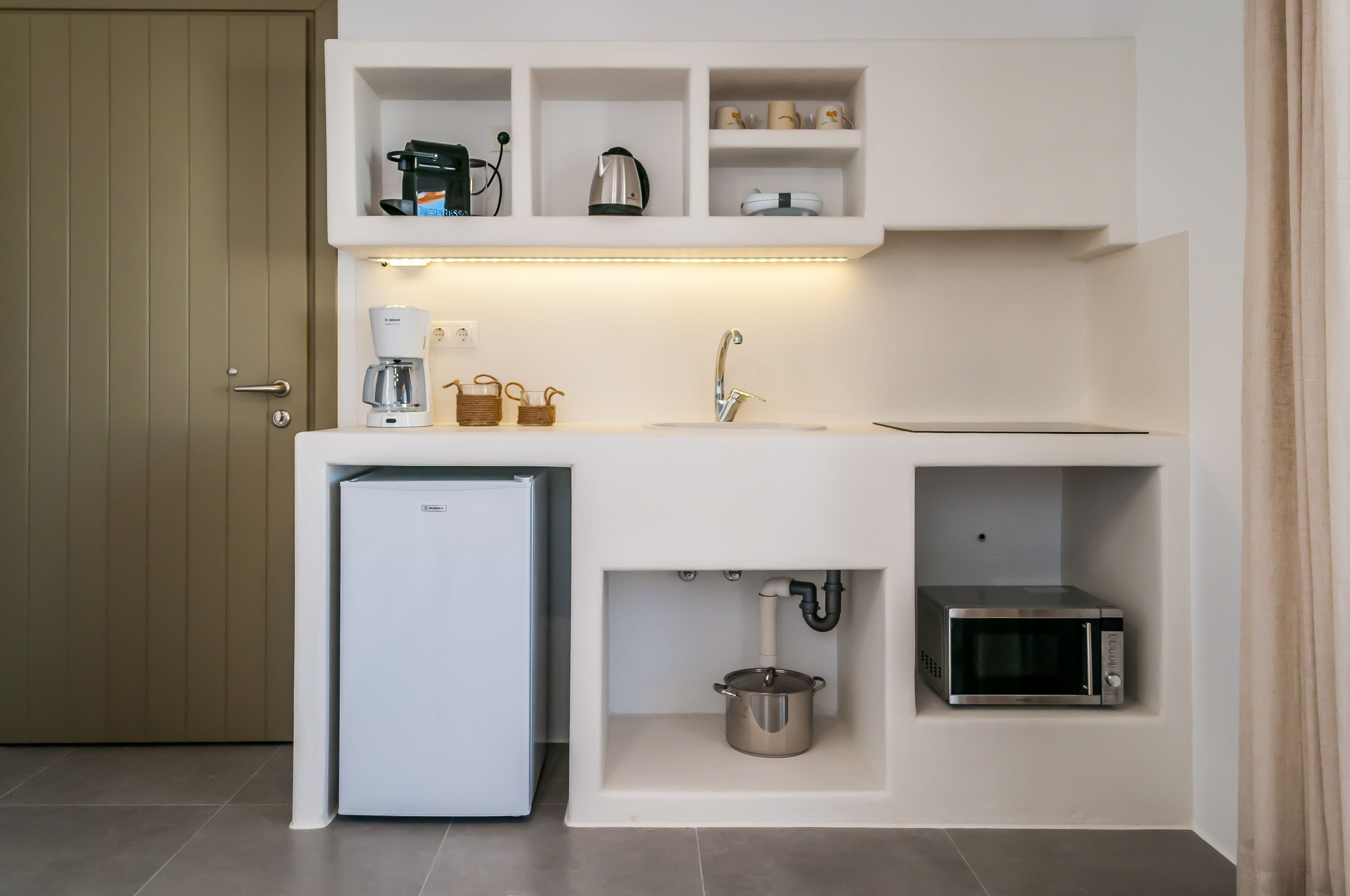 A compact kitchen with a built-in refrigerator, microwave, and sink, featuring under-cabinet storage and a coffee maker.