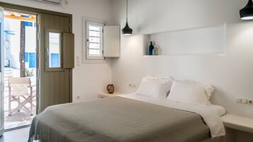 Un dormitorio con cama, mesitas de noche, una ventana y una puerta que da a un espacio exterior.