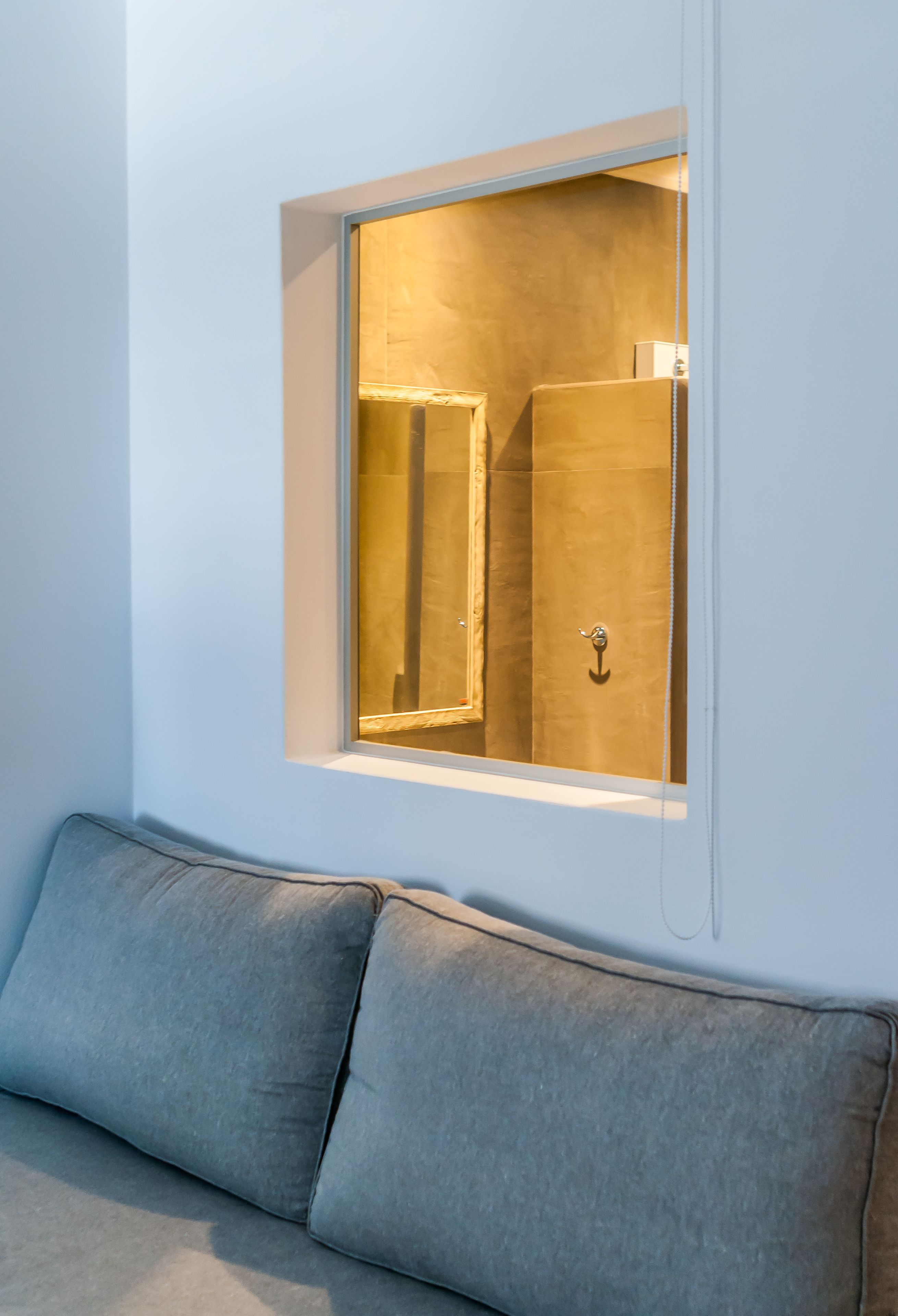A room with a window revealing a bathroom with a towel rack and a door.