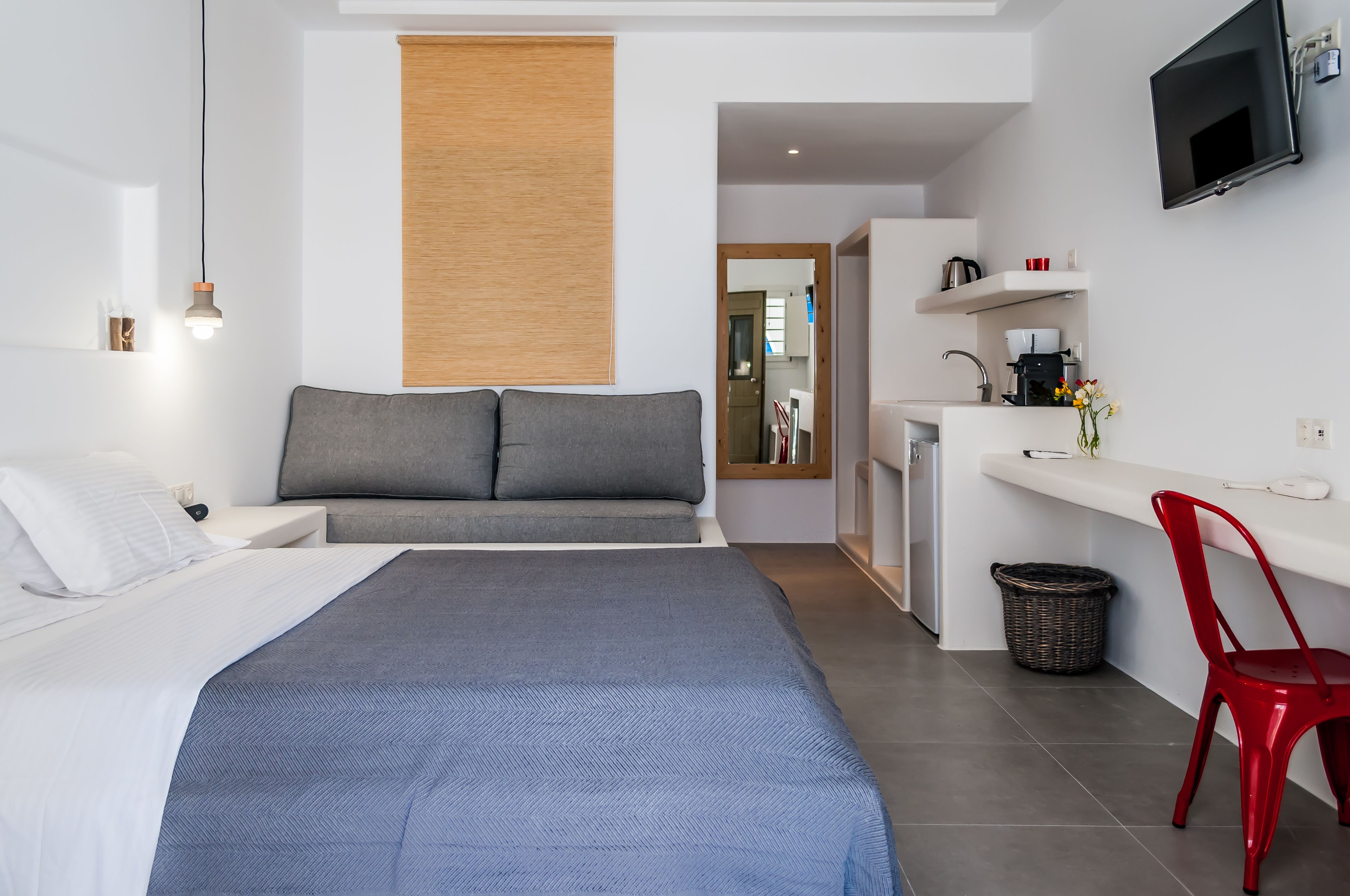 Una habitación de hotel moderna con una cama, un escritorio, una silla roja y un televisor montado en la pared.