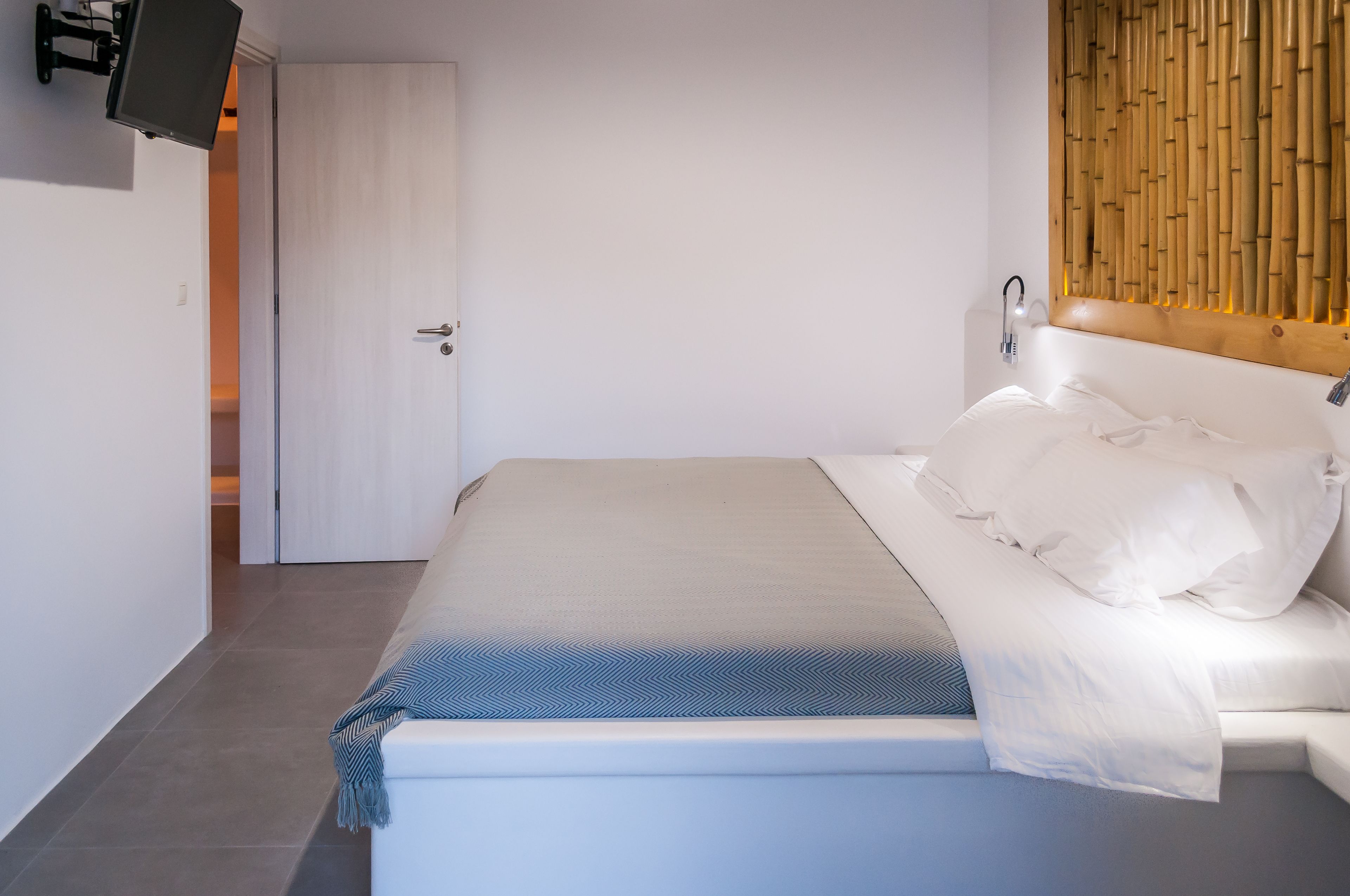 Ein ordentlich bezogenes Bett mit weißen Laken und einer blauen Decke, ein Holz-Kopfteil und ein an der Wand befestigtes Fernsehgerät.