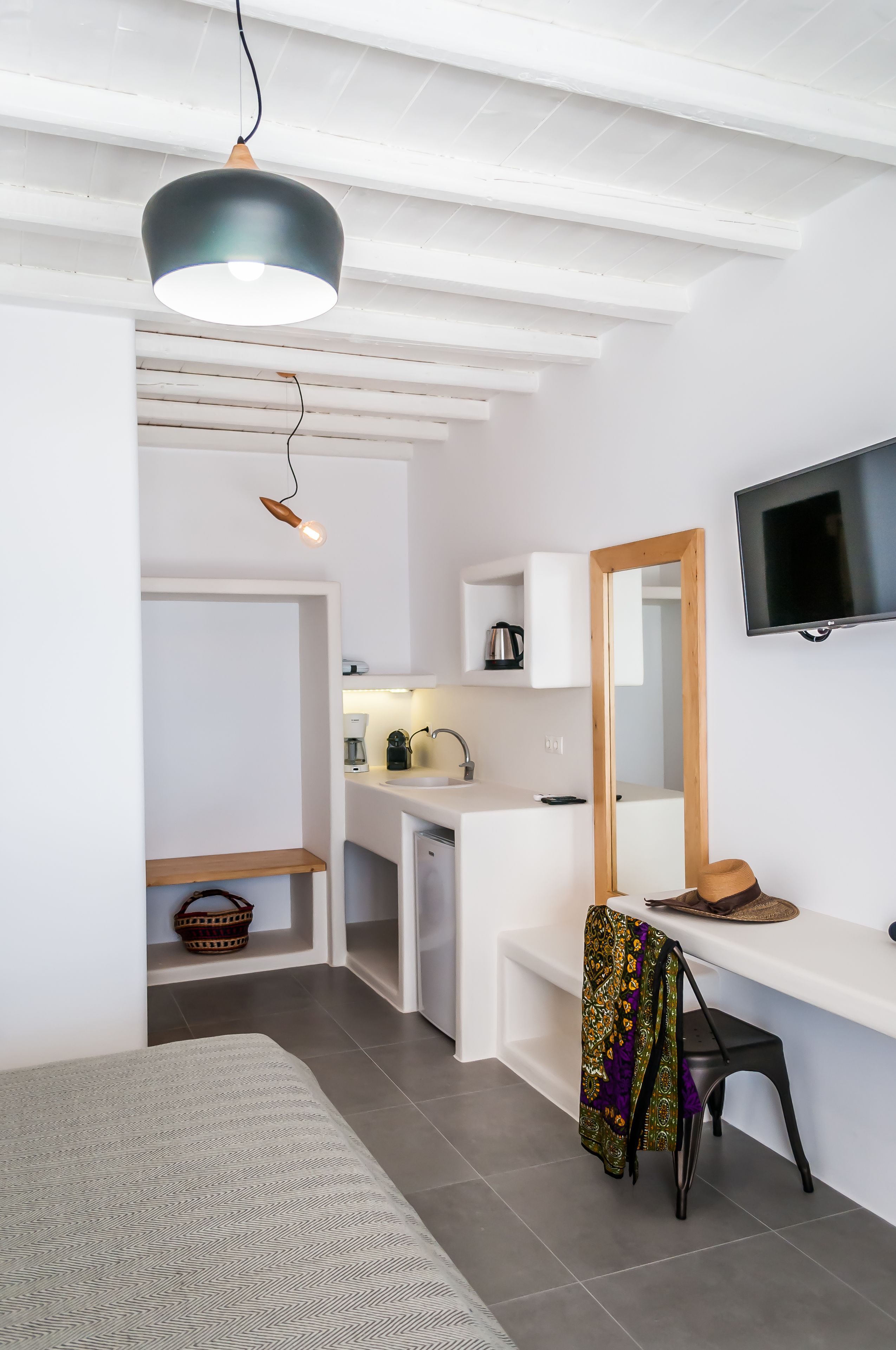 A compact, modern room with a bed, a desk, a chair, a television, and a kitchenette.