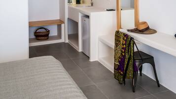 A compact, modern room with a bed, a desk, a chair, a television, and a kitchenette.