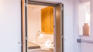 A room with a wooden ceiling, a bed with white bedding, and a wooden panel wall. - Vilos Suites (Milos)
