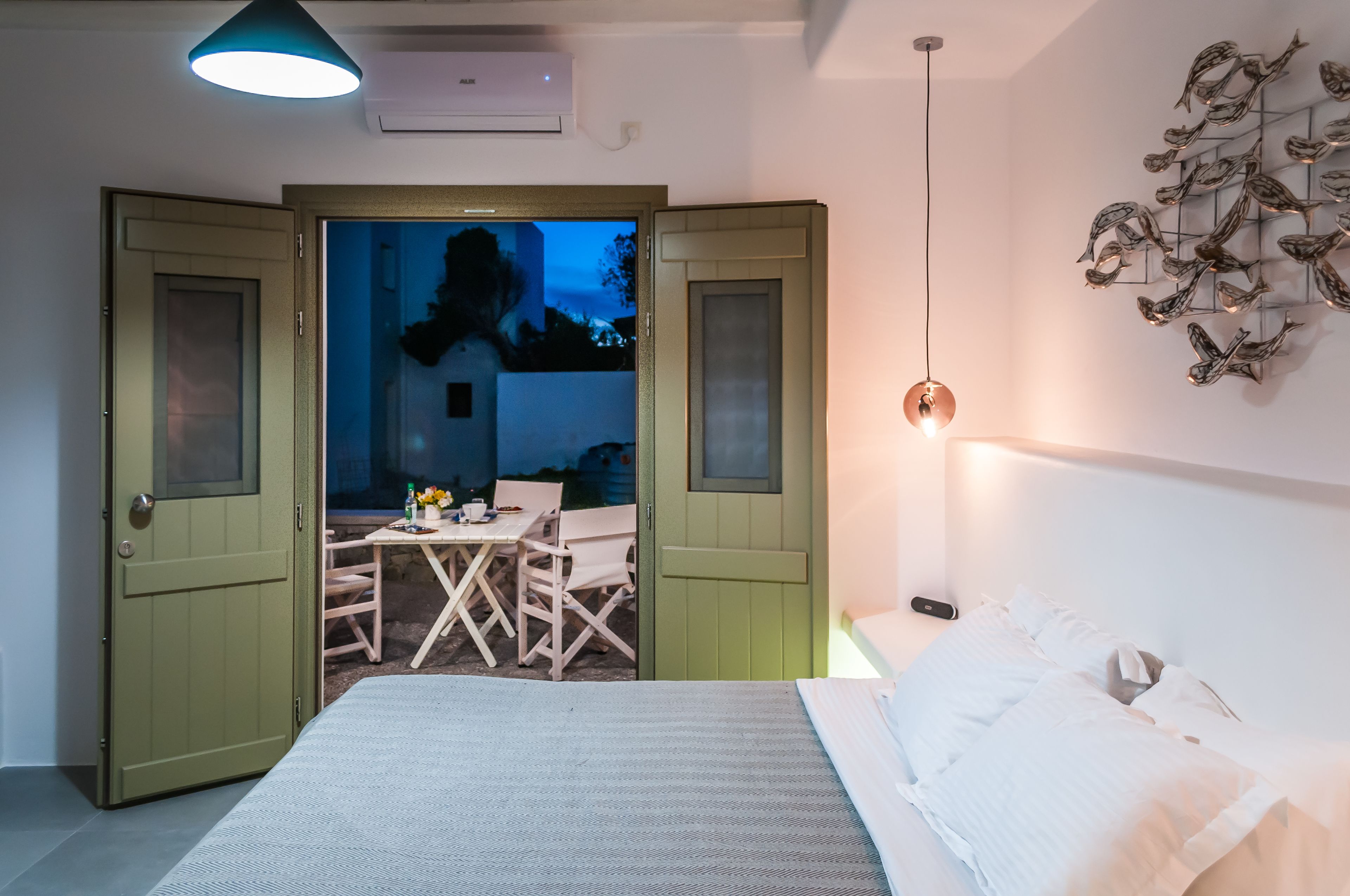 Une chambre avec un lit, une table et des chaises, et une vue sur un espace extérieur accessible par une porte ouverte.