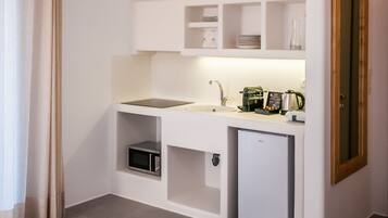 A compact kitchen with white cabinets, a sink, a coffee maker, and a small refrigerator. There is a wooden table with a metal bowl in the foreground.