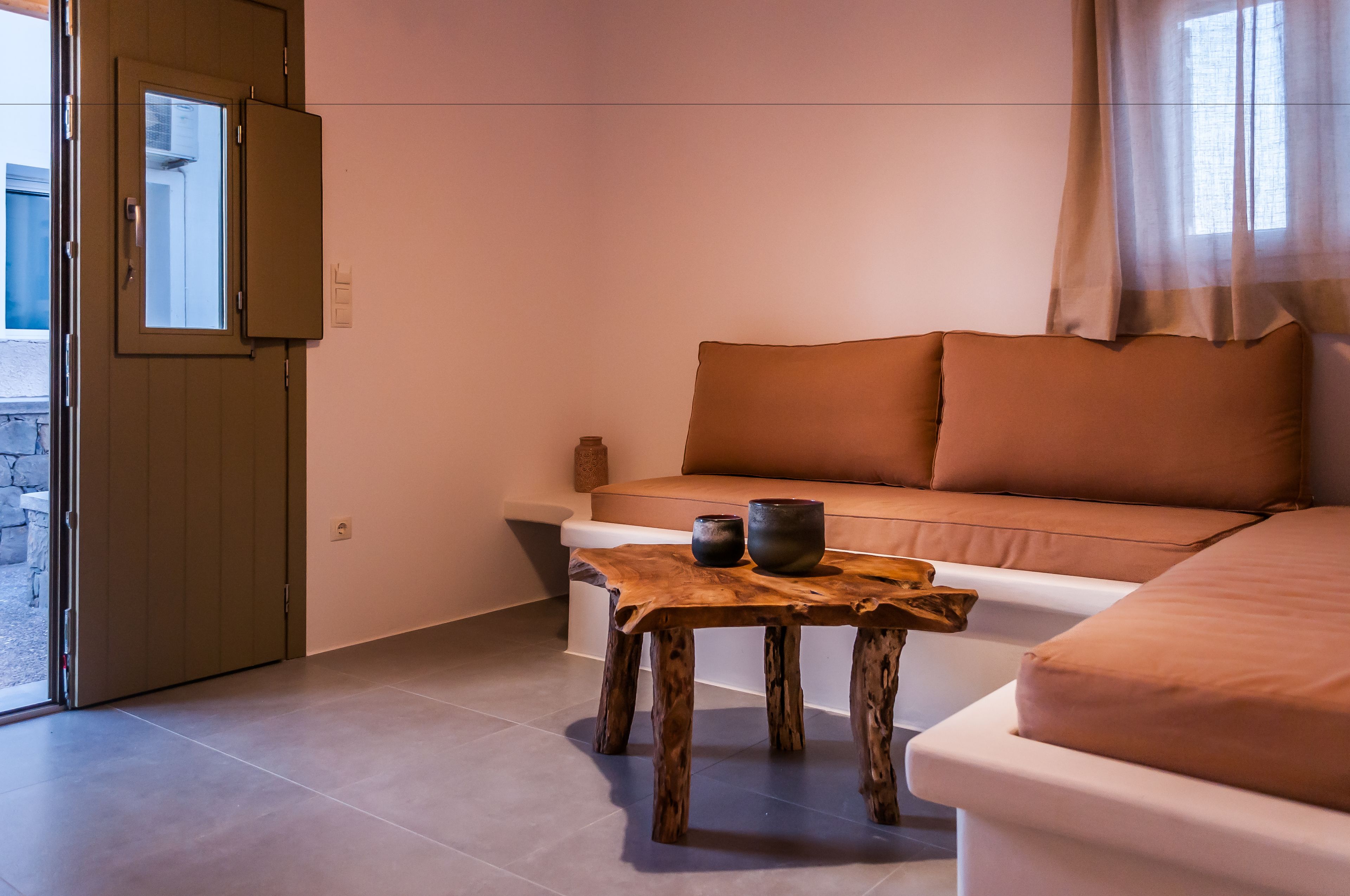 Ein gemütliches Zimmer mit einer Couch, einem Holztisch mit zwei Schalen und einem Fenster mit durchsichtigen Vorhängen.