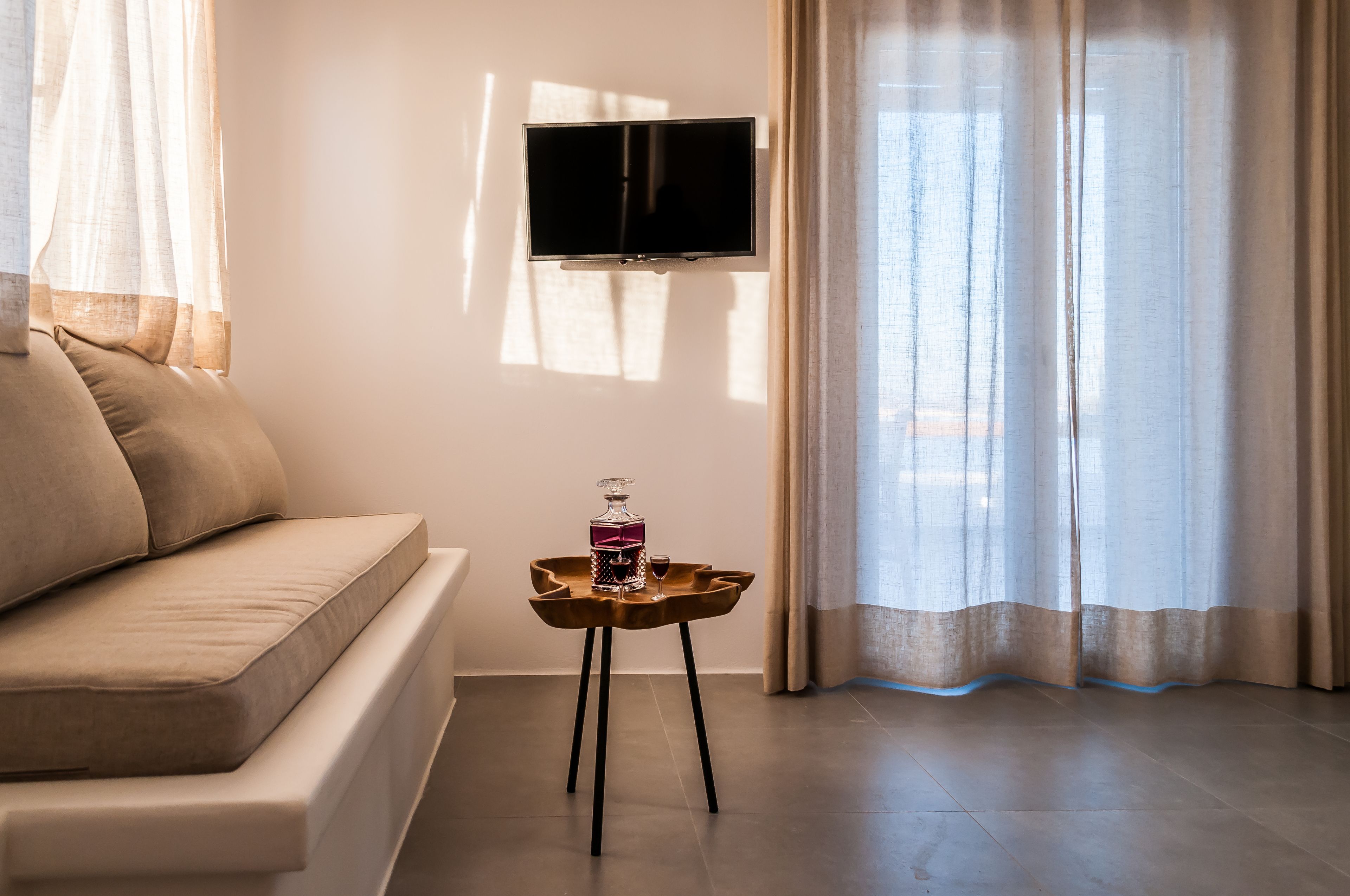 Una sala de estar moderna con un sofá, una pequeña mesita de madera con una botella y un vaso, y un televisor de pantalla plana montado en la pared.