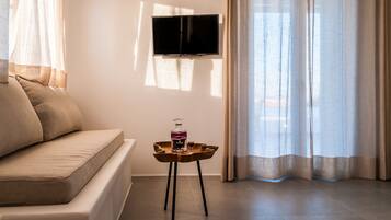 Una sala de estar moderna con un sofá, una pequeña mesita de madera con una botella y un vaso, y un televisor de pantalla plana montado en la pared.