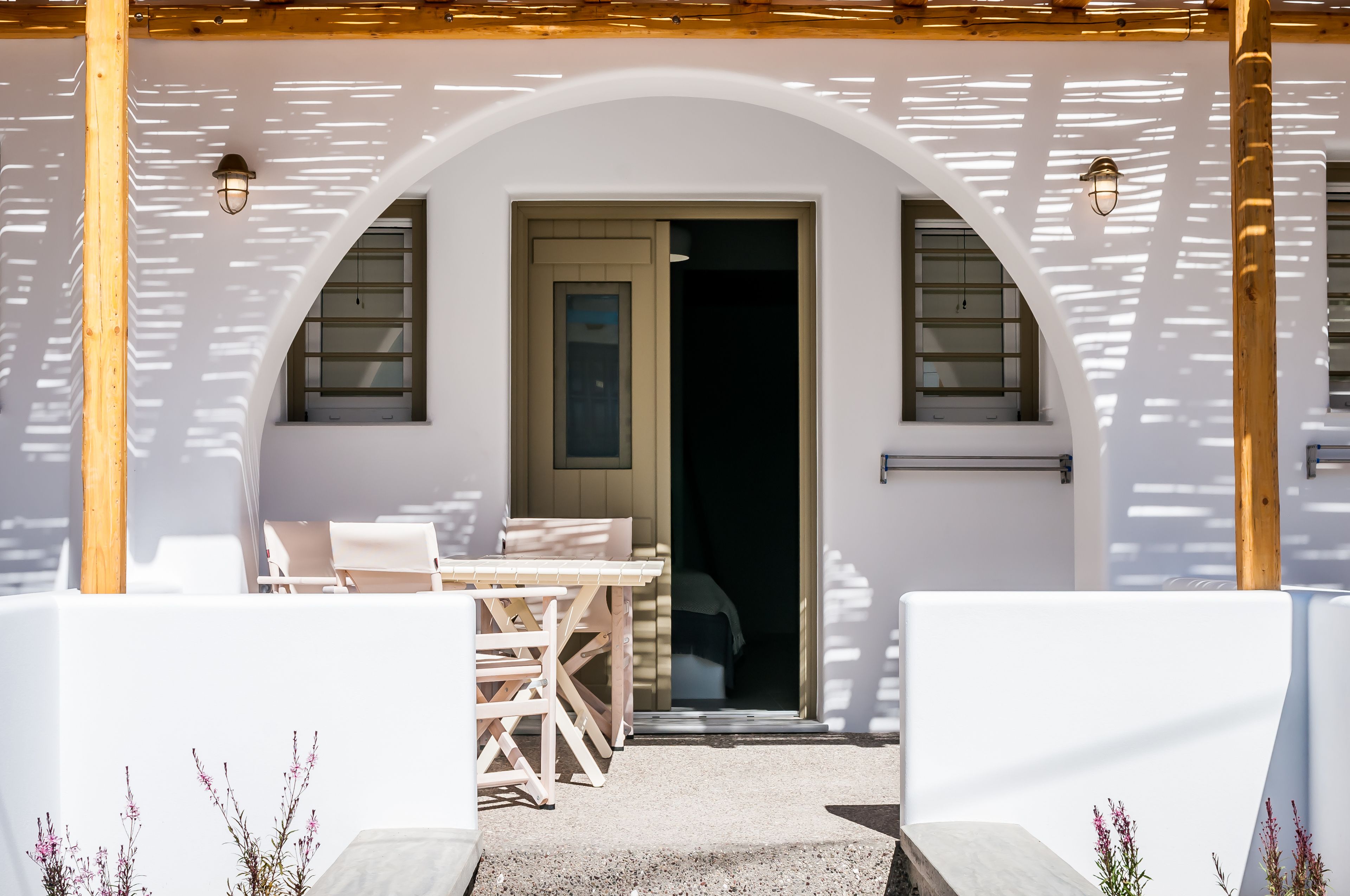 A white building with an arched entrance, wooden beams, and a table with chairs outside.