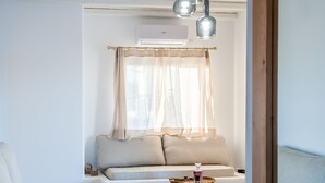 A modern living room with a white sofa, a wooden stool, and a small table with a tray. - Vilos Suites (Milos)