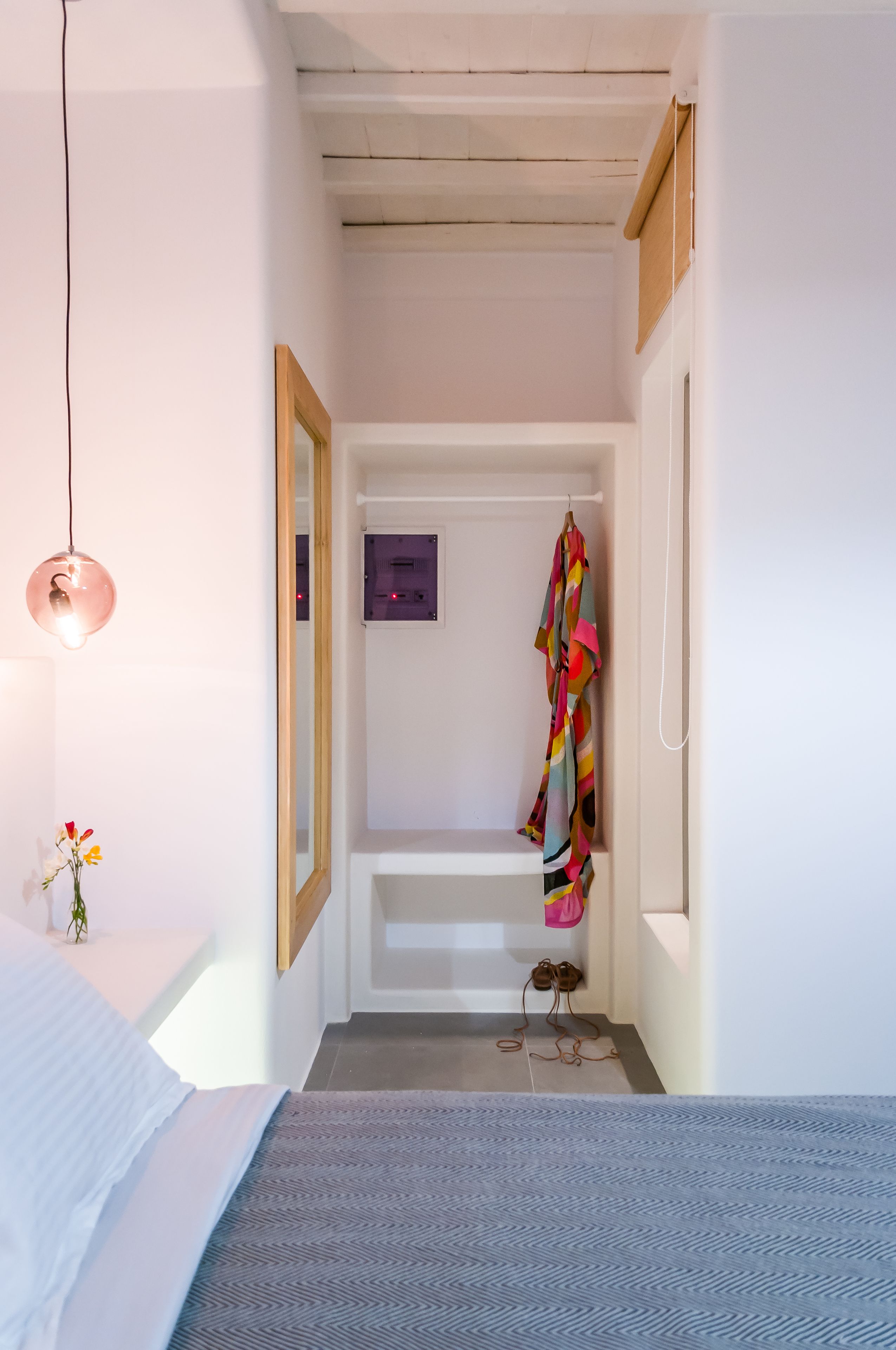 Un pasillo estrecho con una cama a la izquierda, una lámpara colgante y una prenda de vestir colorida en un gancho.