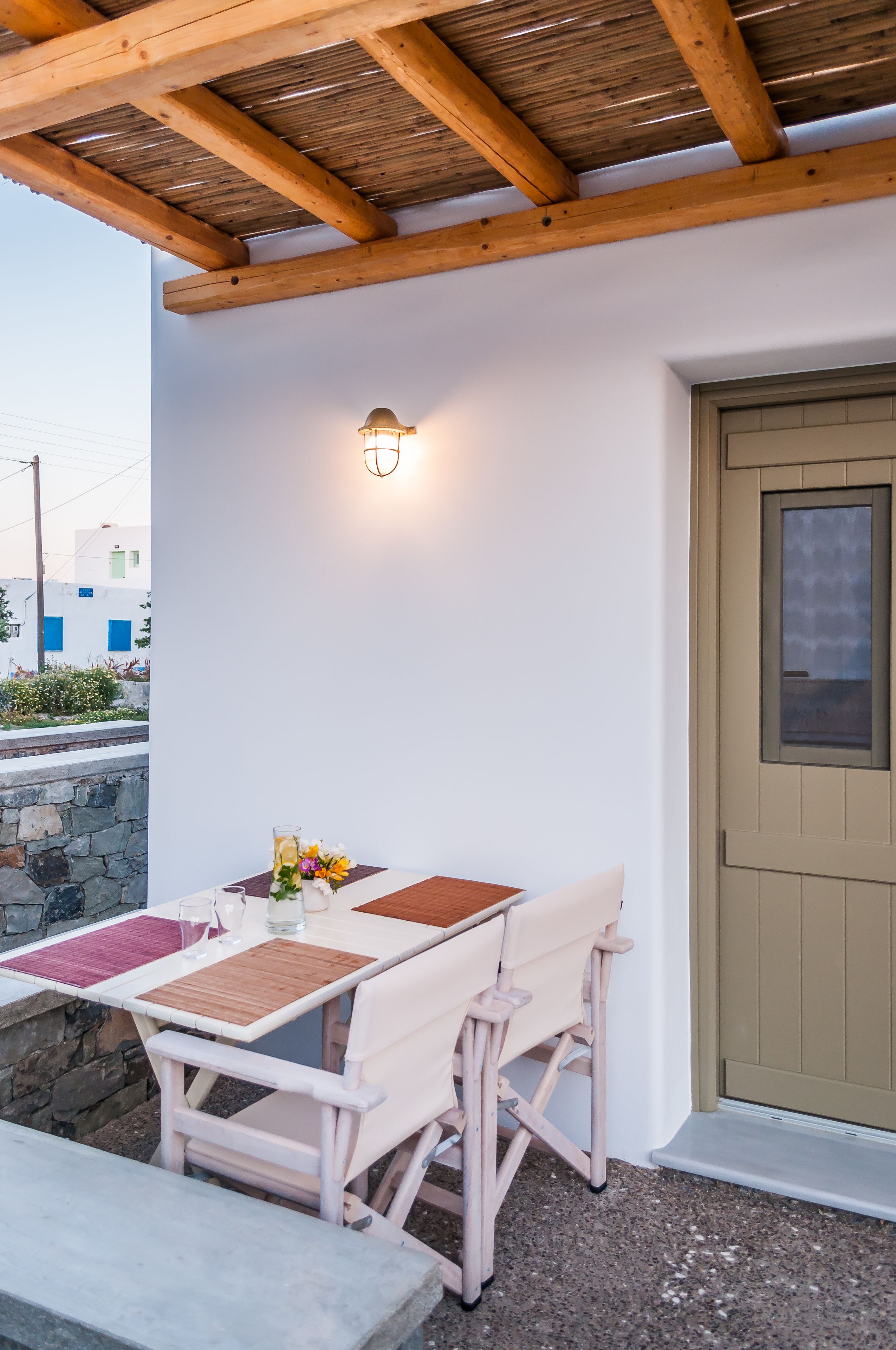 Un espacio de estar al aire libre con techo, una mesa, sillas, una lámpara y una puerta.