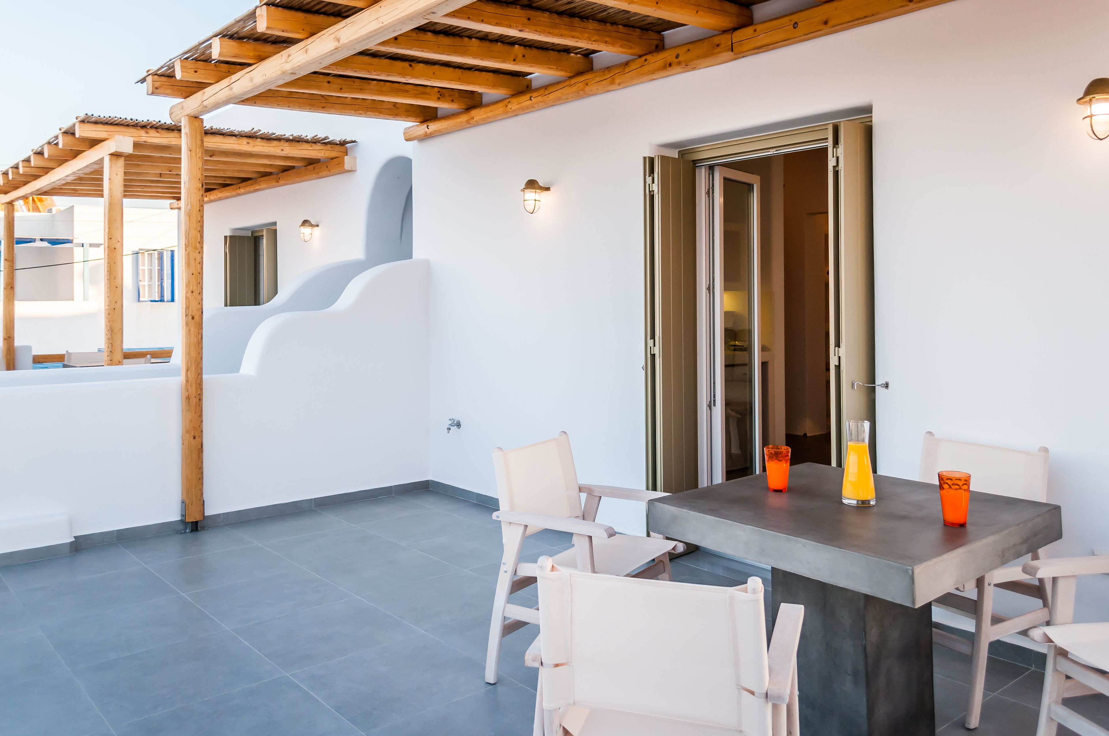 Une terrasse extérieure moderne, dotée d’une pergola en bois, d’une table avec des chaises et d’une porte vitrée donnant sur l’intérieur.
