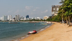A beach with a jet ski on the sand, boats in the water, and a city skyline in the background. - The Classroom Hotel (Pattaya)