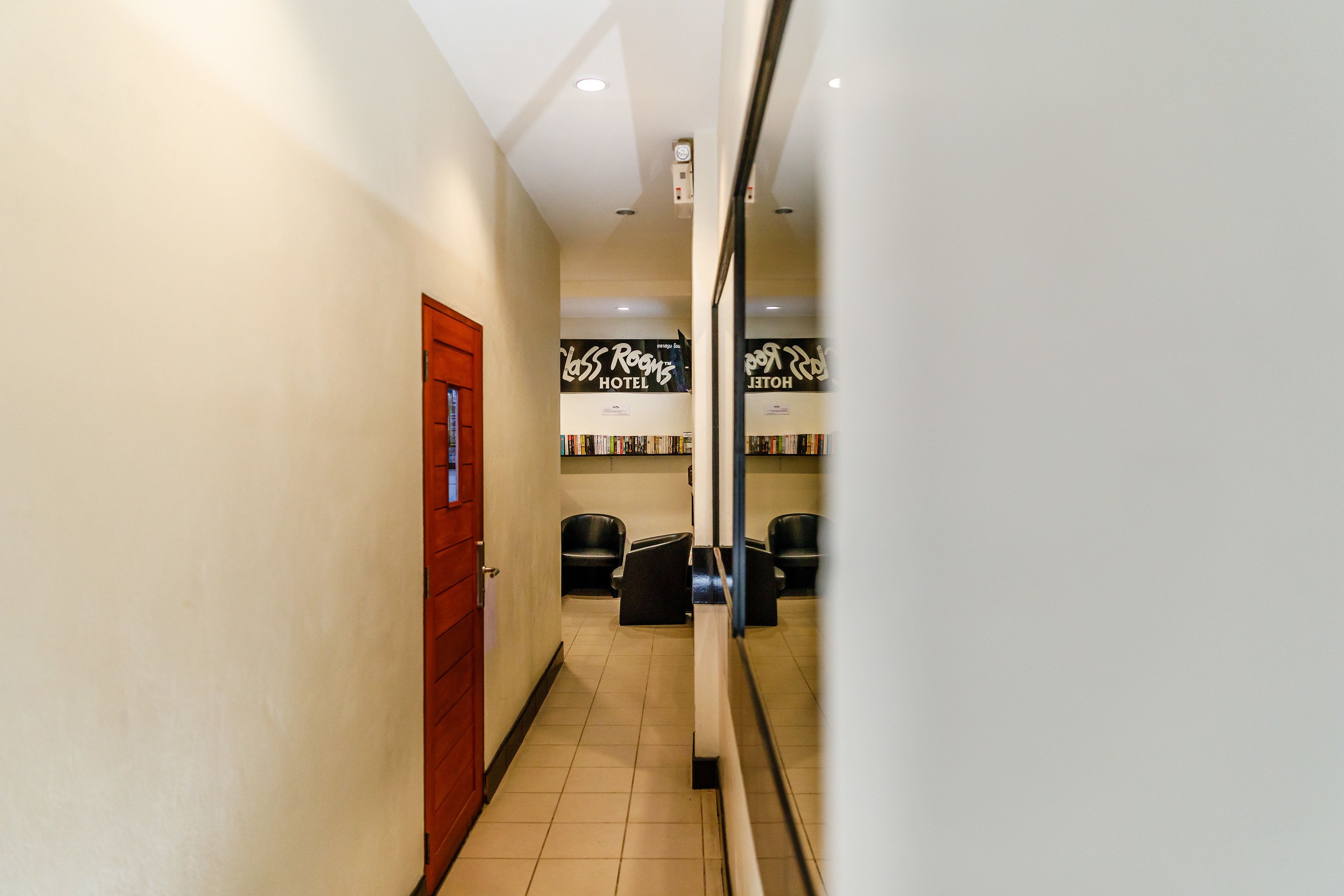 Ein Hotelkorridor mit einer roten Tür, einem Empfangstresen und einer Spiegelwand, die die Raumschilder reflektiert.