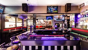 A bar area with a counter, seating, and a television screen. - The Classroom Hotel (Pattaya)