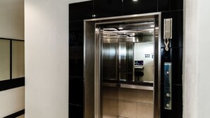 An elevator with a metallic interior, a handrail, and a control panel with a button. - The Classroom Hotel (Pattaya)