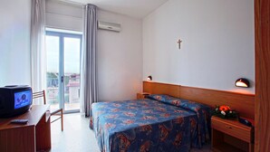 Habitación de hotel con cama, escritorio con televisor, mesita de noche con lámpara y ventana con cortinas.