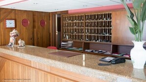 Un área de recepción con mostrador de madera, una vitrina con trofeos, un reloj y un florero con planta.