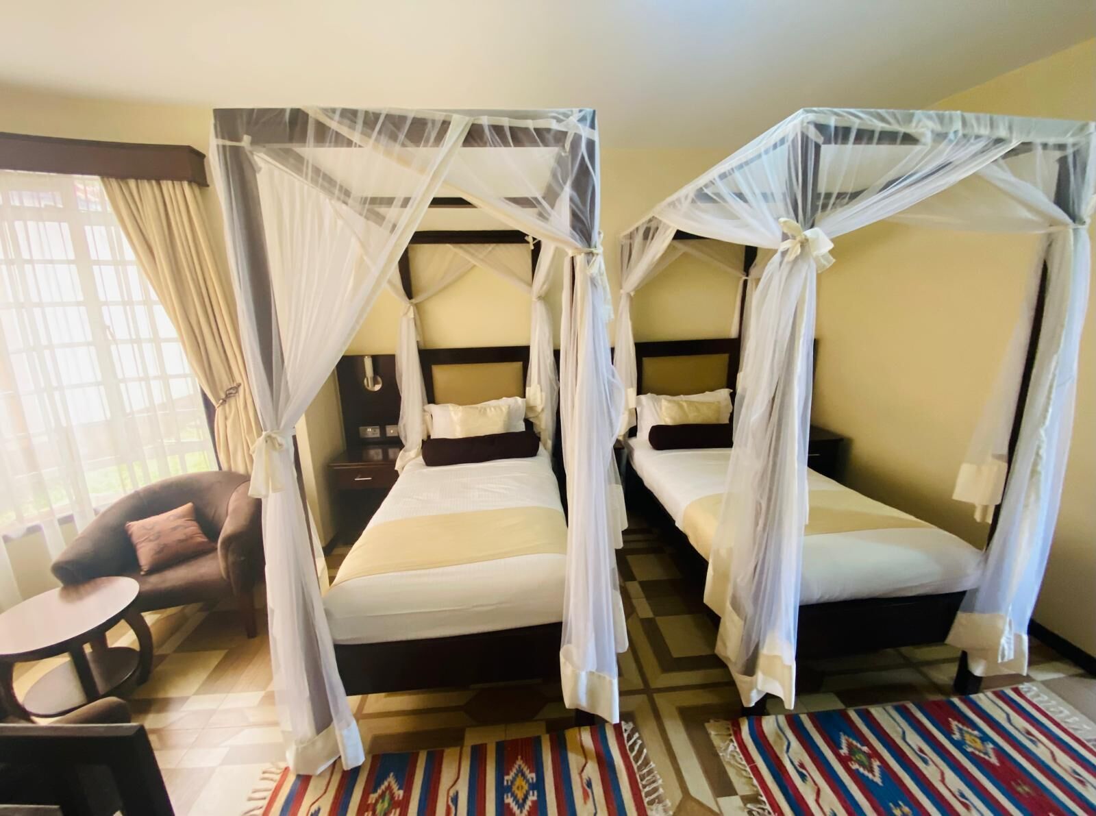 Une chambre d’hôtel avec deux lits, chacun surmonté d’un baldaquin, une petite table ronde et un tapis à motifs.