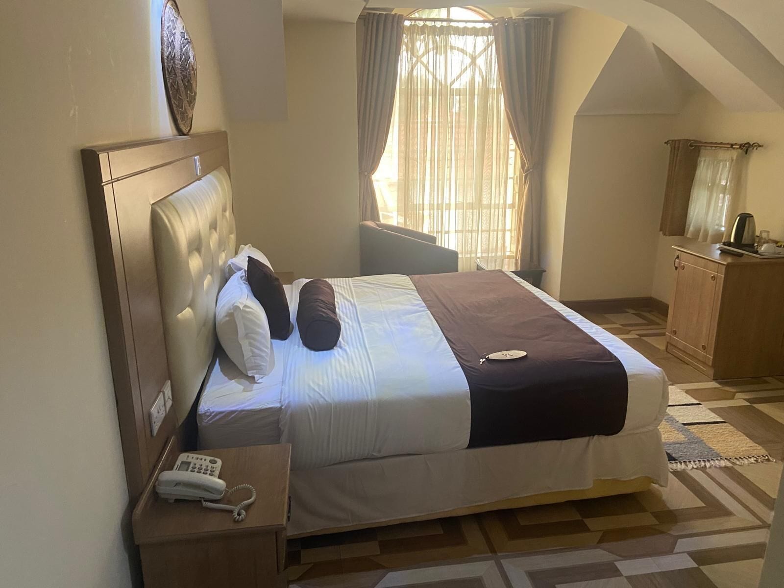 Quarto com cama, mesa de cabeceira com telefone, janela com cortinas e um armário de madeira.