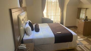 Quarto com cama, mesa de cabeceira com telefone, janela com cortinas e um armário de madeira.
